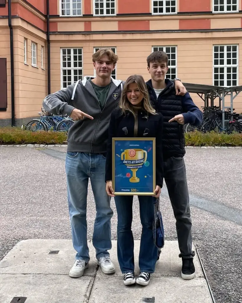 Tre personer med skylt "Årets Affärssida". Hus och cyklar i bakgrunden